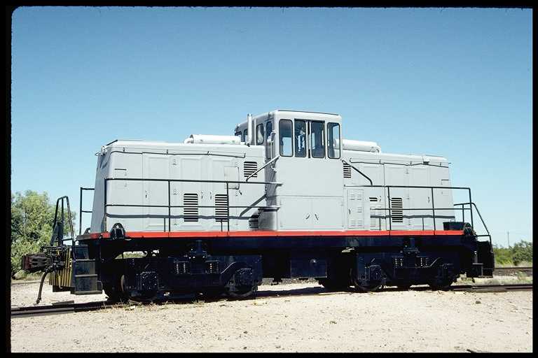 Center cab locomotive being delivered by flatcar.  Still in gray primer paint.